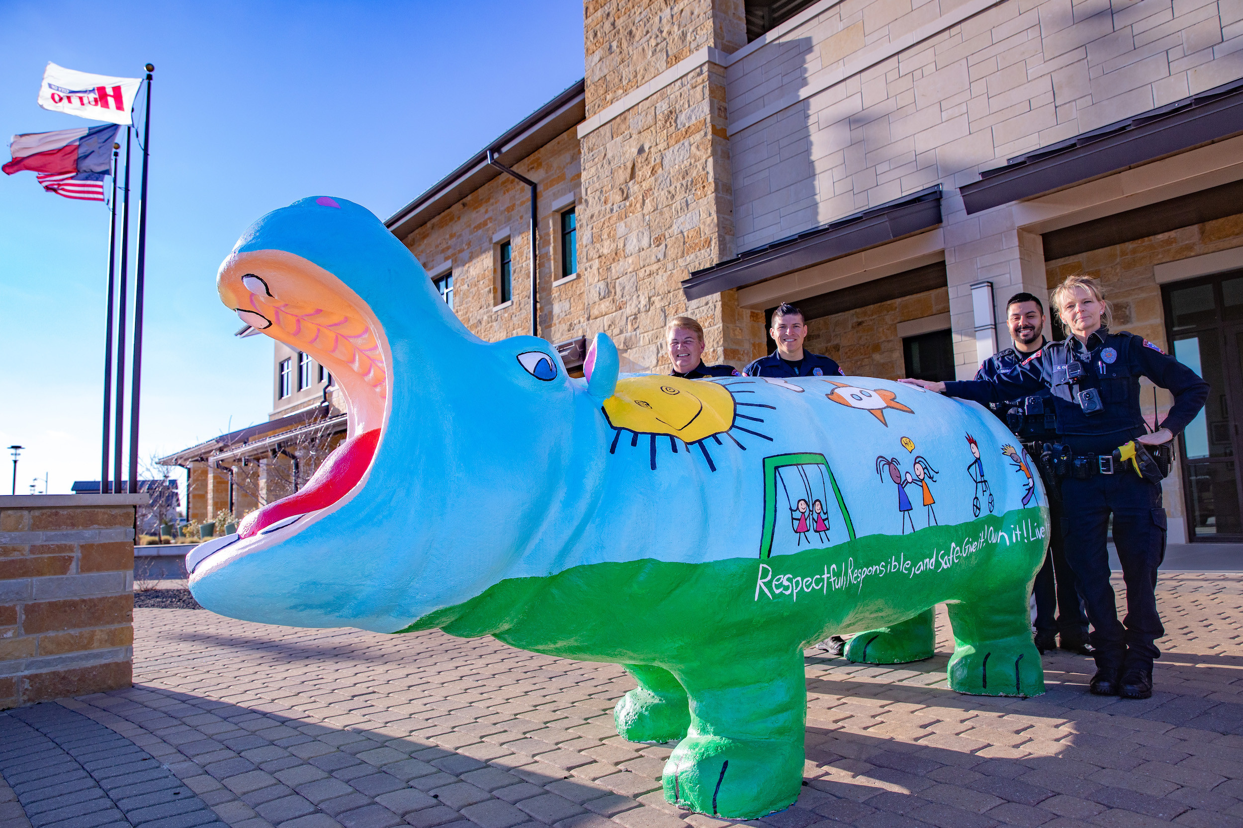 Photo of police officers standing with a concrete hippo painted with children playing outside